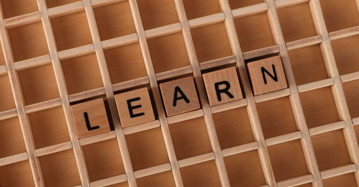 Wooden letter blocks spelling 'Learn' placed on a wooden grid background.